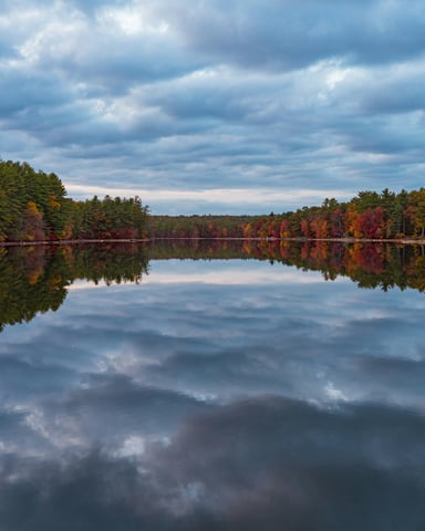 Still New England pond perfectly reflecting autumn foliage and dramatic clouds overhead