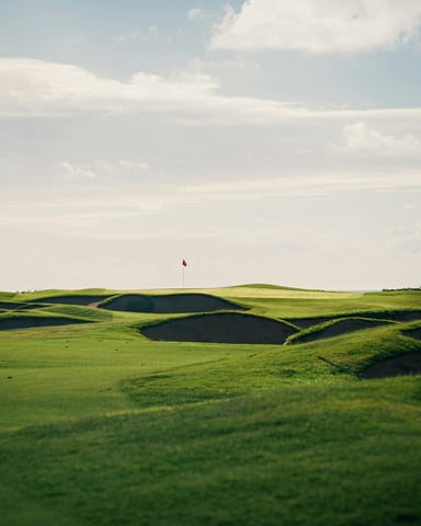 Wide open golf course with undulating fairways, sand bunkers, and a flag in the distance
