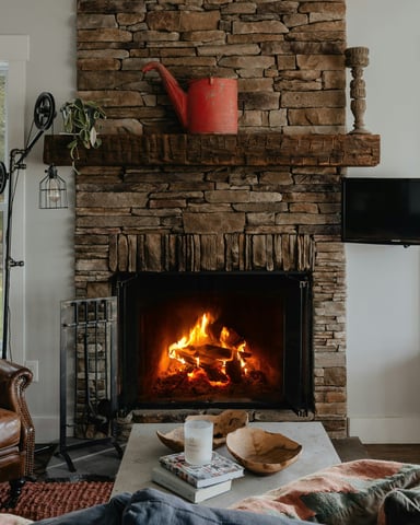 Stone fireplace blazing in a cottage living room with leather armchair and winter light through the windows