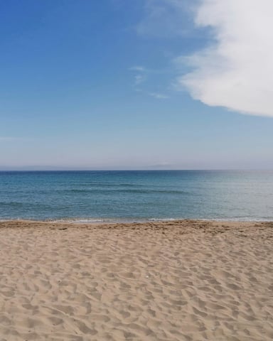 Wide open sandy beach with calm blue water and a clear sky
