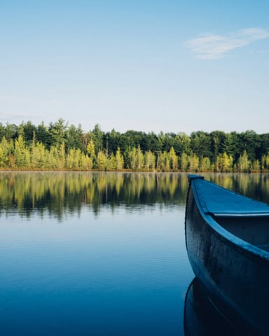 Calm pine-fringed lake with a canoe bow in the foreground and clear blue sky above