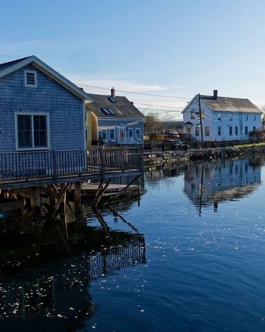 Cedar-shingled harbor buildings reflected in still blue water at golden hour on a quiet Cape Cod winter day
