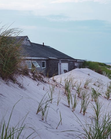 Cape Cod dune cottage on a wide sandy beach with sea grass blowing in the breeze