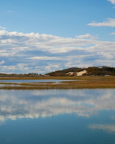 Calm tidal water reflecting blue sky over Cape Cod salt marsh and sand dunes