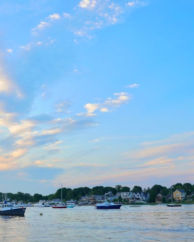 Boats moored in a New England harbor at sunset with houses and trees along the shoreline
