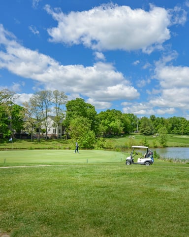 Sunny golf course with a cart path, pond, and lush green fairway under a blue sky