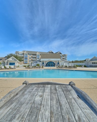 Outdoor resort pool with New England-style shingled buildings and lounge chairs under a wide blue sky