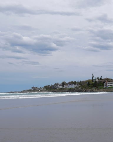 Wide sandy beach with resort buildings along the shoreline under a cloudy Cape Cod sky