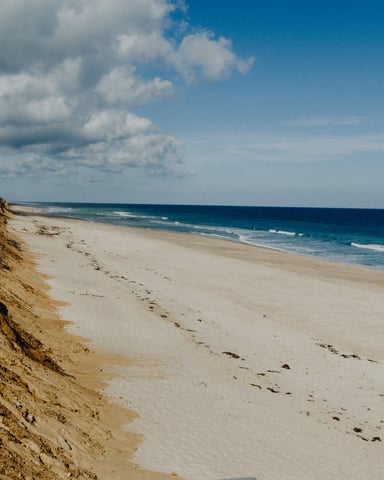 Wide empty Cape Cod beach with tall eroded sand dunes and blue sky