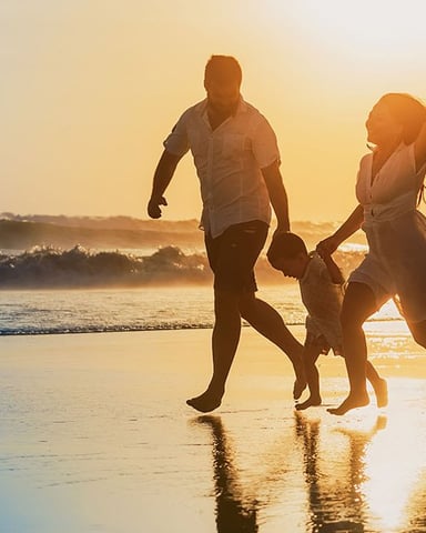 Family of four running together in shallow ocean water at golden-hour sunset