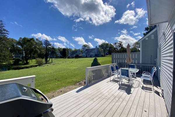 Deck with dining furniture and umbrella overlooking a wide Cape Cod lawn