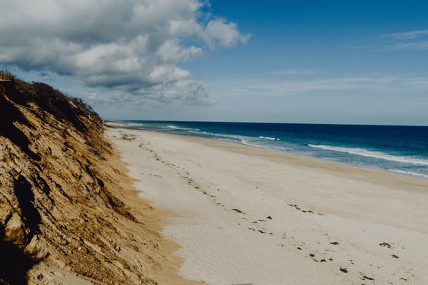Wide empty Cape Cod beach with tall eroded Atlantic dunes under a blue sky