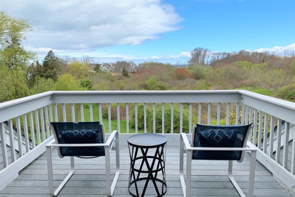 Elevated deck with two white chairs overlooking a wooded Cape Cod neighborhood
