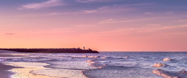 Family of four running together in shallow ocean water at sunset
