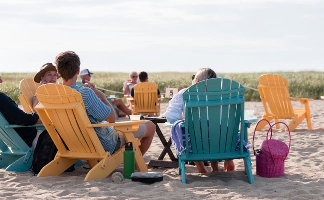 Families relaxing in colorful Adirondack chairs on a Cape Cod beach