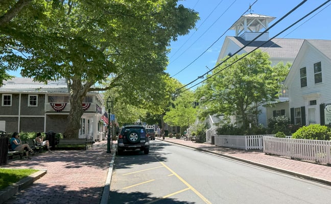 Tree-lined main street in a Cape Cod village with white clapboard buildings on a sunny day