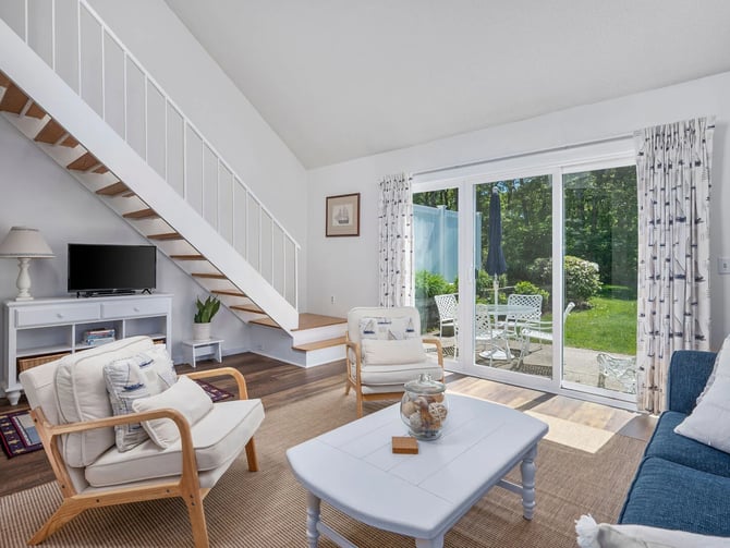 Bright Cape Cod condo living room with staircase and sliding doors to a patio garden